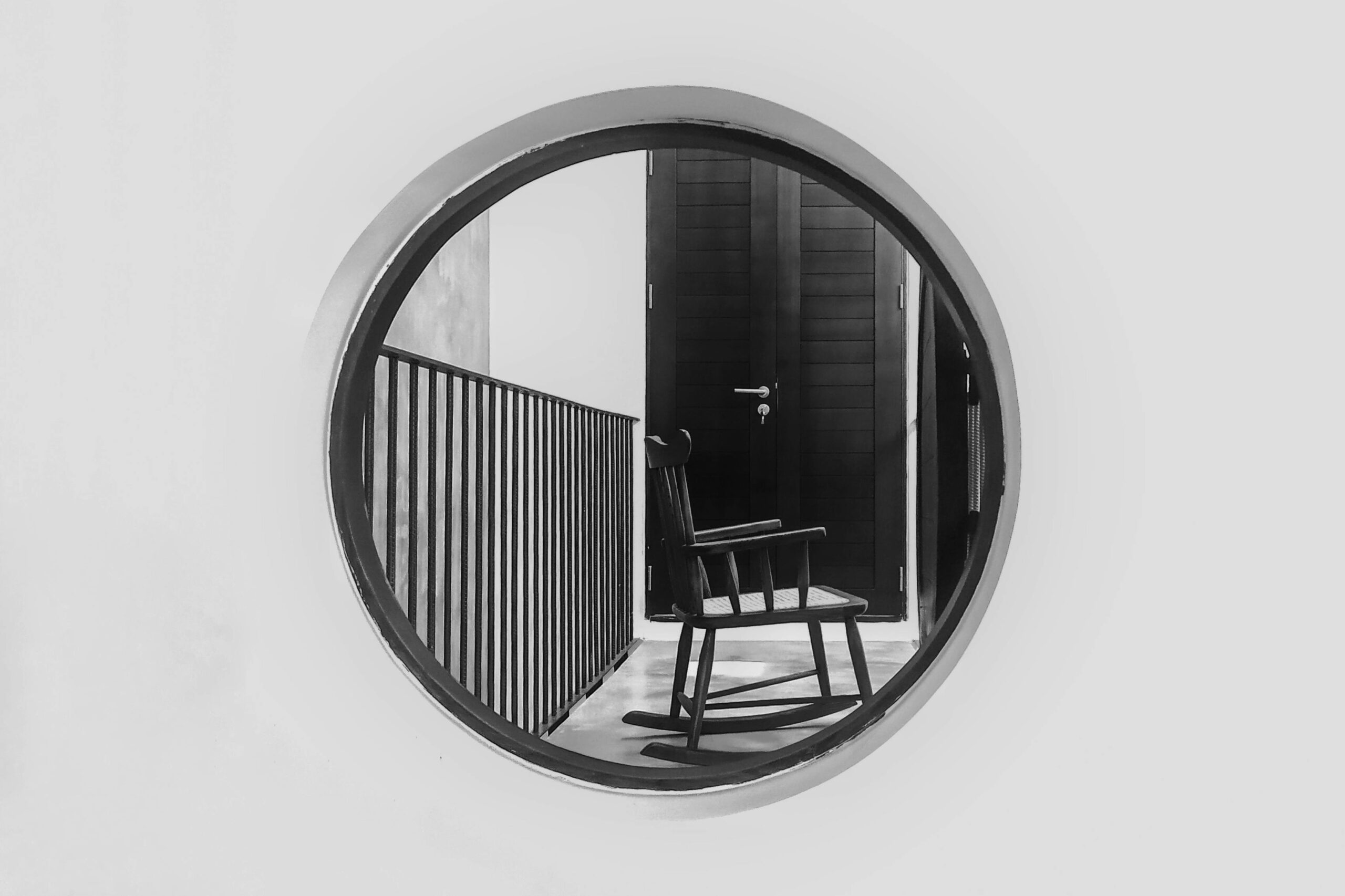 Black and white image of a rocking chair framed by a circular opening against a minimalistic indoor setting.